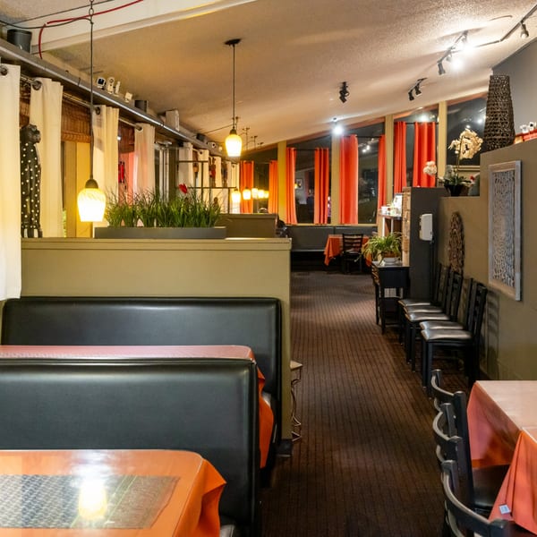Interior of Tasty Thai Kitchen with booths, tables, orange tablecloths, and red curtains.