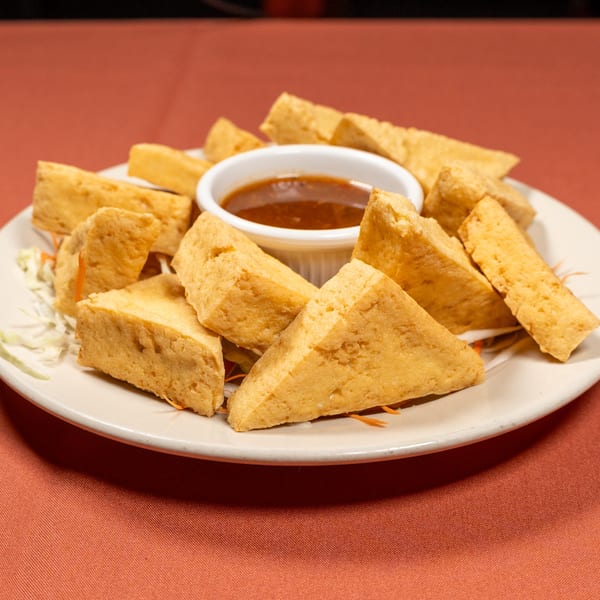 Crispy fried tofu triangles with a sweet and sour dipping sauce on a white plate.