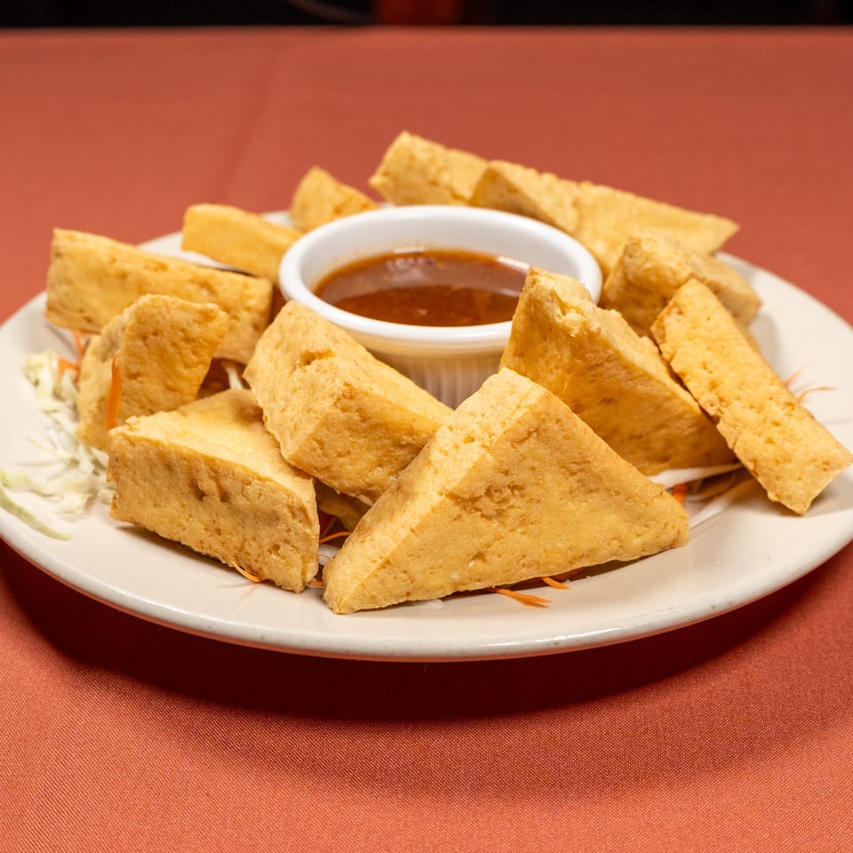 Crispy fried tofu triangles with a sweet and sour dipping sauce on a white plate.